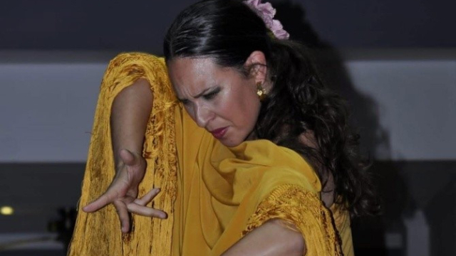 Bailaora de flamenco con vestido amarillo y mantón de flecos, realizando una pose expresiva durante una actuación